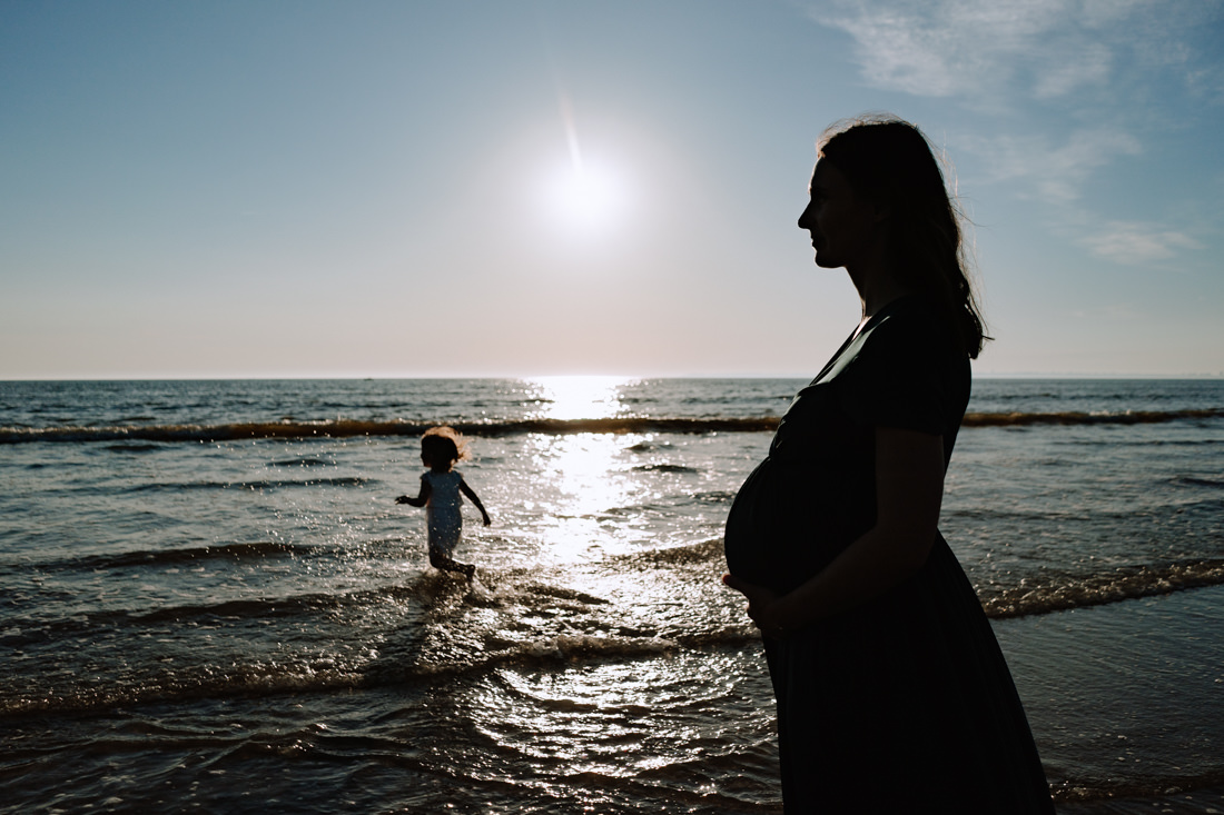 enfant courant dans les vague avec sa maman enceinte devant